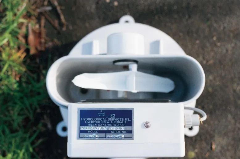 Top view of a tipping bucket rain gauge and data logger. It looks like a small plastic seesaw inside a stadium-shaped container.