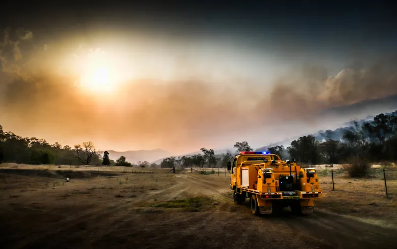 Bright orange emergency vehicle on a dusty dirt road with a smoky and hazy sky obscuring the sun in the background.
