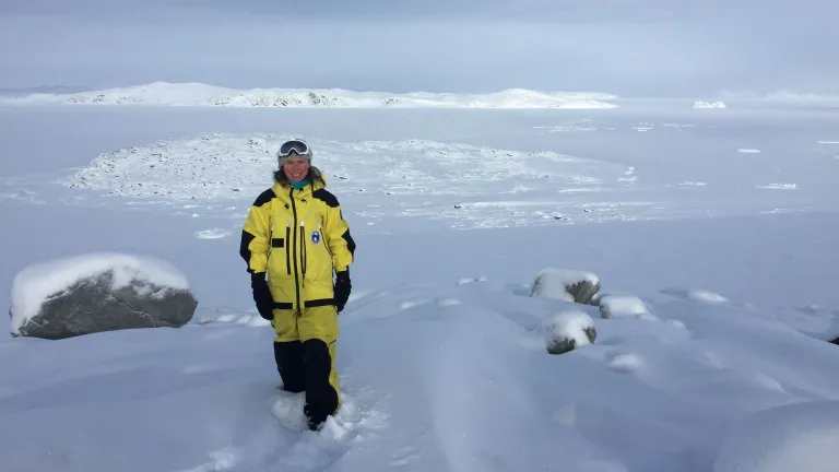 Woman in yellow waterproof gear stands in a landscape of ice and snow.